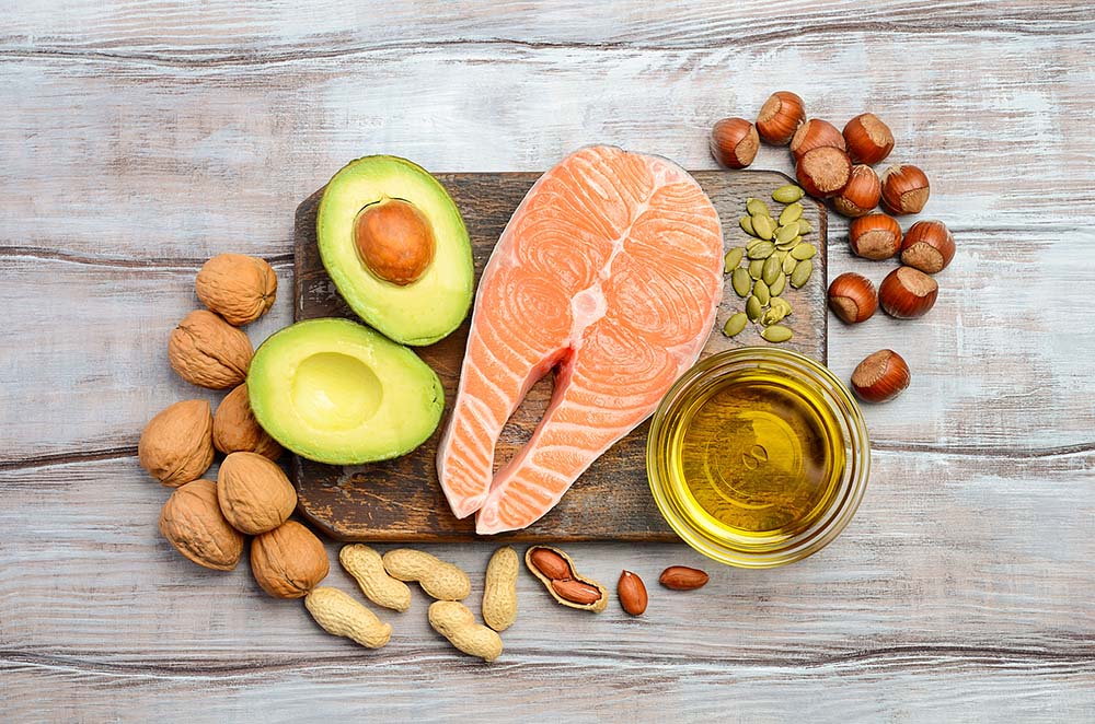 A plate of avocados, salmon, nuts, and olive oil showing healthy fats and oils